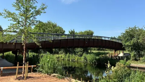 George Torr/BBC A bridge stretching across a canal with railings at the side. Lots of greenery can be seen in the image.