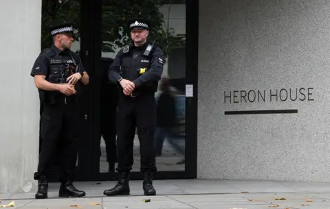 Ryan Jenkinson / Getty Images Two police officers stand in front of the entrance to a building with lettering that reads 'Heron House', in Manchester on 23 July.