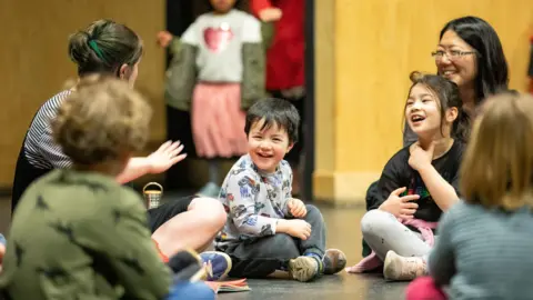 Sara Beaumont/RSC Children sat on the floor smiling and listening to group leader 