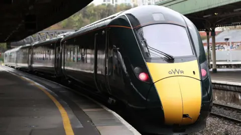 A dark green Great Western Railway train pulls up to an empty train platform at Bristol Temple Meads.