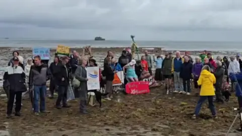 Protesters gather on the beach with placards.