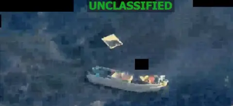 A screengrab from a video posted by US Southern Command shows a small vessel in the sea with what appears to be debris floating nearby. The word "unclassified" has been printed on top of the footage.