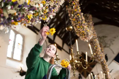 A person putting a flower on the garland, wearing a green jumper