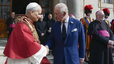 EPA/Shutterstock Pope Leo XIV cloaked in red shaking hands with King Charles in a blue suit outside the Sistine Chapel