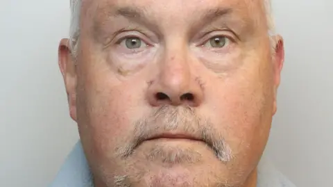 Wiltshire Police Headshot of an older man with short white hair and a grey thinning moustache and goatee beard. 