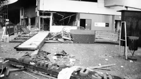 Getty Images The remains of a pub after a bombing, showing blown out windows on the ground floor, hanging rafters and debris spilling into the street. An external wall sign saying Brew is just visible on a corner leading away from the main door. The pub's main sign lies on the floor in the foreground, broken so only some of the letters can be seen.
