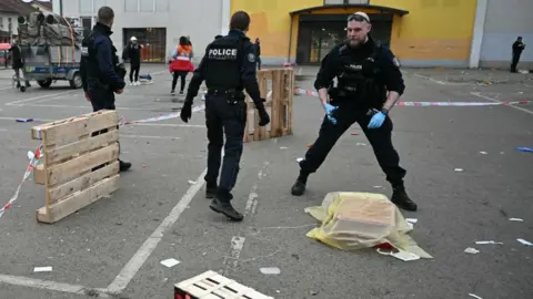 Getty Images Seorang petugas polisi mengumpulkan bukti dalam apa yang tampak seperti tempat parkir, pada hari yang kelabu dan suram. 