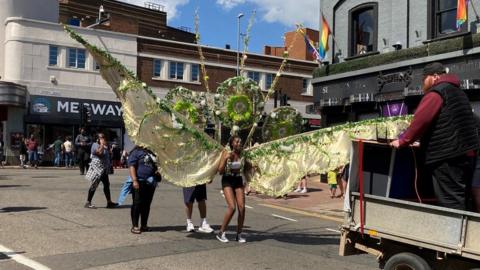 Carnival parade with woman wearing huge yellow wings in the foreground