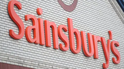 PA Media A close-up of the Sainsbury's sign, on the wall of a store