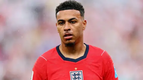 Reuters Morgan Rogers standing on the pitch while wearing a red England shirt.