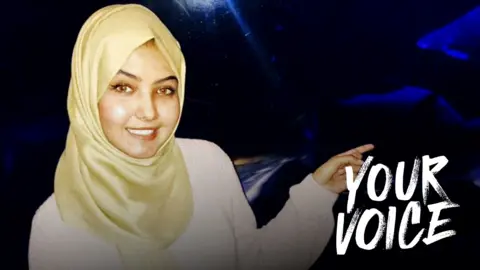 Susan Nasser wearing a cream top and light yellow hijab, smiling and pointing to the side against a dark background. The words YOUR VOICE have been imposed on the photo on the right hand side.