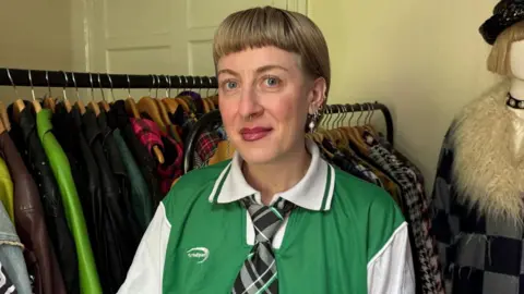 BBC is a short blond hair woman standing in front of the bars of the jackets