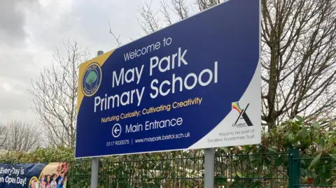 The sign at the front of May Park primary school bearing its name and logo which is a tree in a circular badge