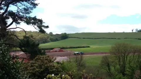 Fields at the Wolborough site showing where excavation work has been carried out with a tractor driving along a mud path