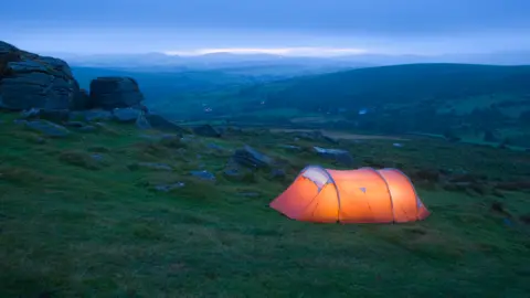 An orange tent lit from inside on Dartmoor moorland at dusk.