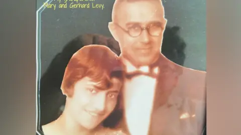 Adrian Kriss An old photo shows Mrs Levy with short red hair stood next to her husband who is wearing a smart suit and bow tie with glasses on.