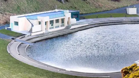 A white restored pavilion next to an open air pool.