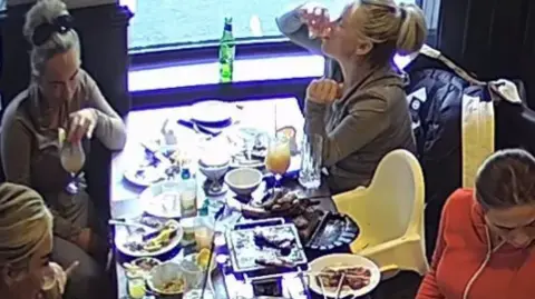 Norfolk Police/Andrea Marinho Four women sit at a table in a restaurant surrounded by plates of food and glasses full of cocktails in CCTV footage
