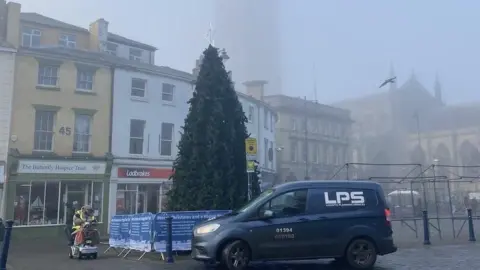 A Christmas tree in a shopping square with a navy coloured transit van parked in front