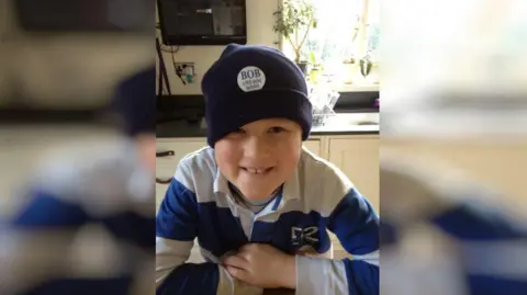 Handout A young boy in a blue beanie hat. He is smiling.