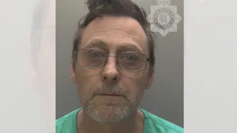 Humberside Police A police custody photograph of a middle-aged man wearing glasses and a green t-shirt. 