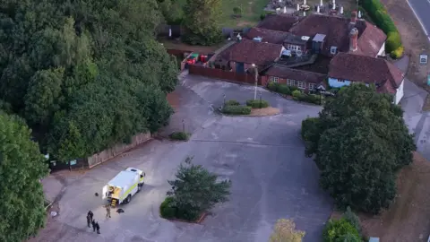 Aerial shot of police officers and vehicle in car park outside a property.