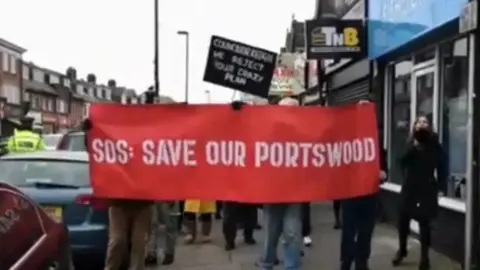 Simon Morice People walking on Portswood road with a red banner reading "SOS: save our Portswood"