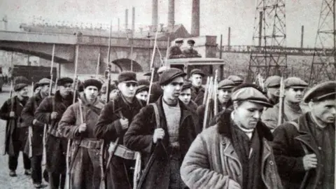 Getty Images A group of men marching while holding rifles in the early 1940s