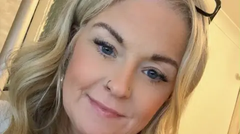 Melanie Stinton takes a selfie. She has curly blonde hair and is wearing her glasses on her head.