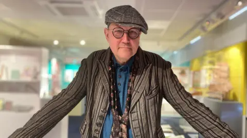 Simon Costin - from the Museum of British Folklore - leaning over a display case, wearing a flatcap and striped jacket