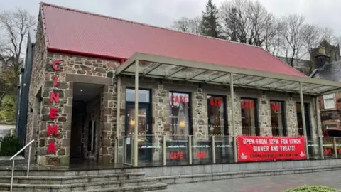 BBC A view of the front of the Highland cinema. It has attractive stone work, large windows and a red corrugated iron roof. 