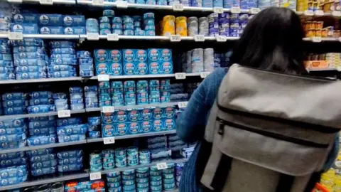 EPA Tinned tuna sits on a shop shelf as a customer looks at it