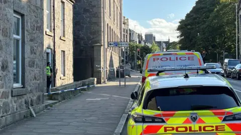 Police officer and police vehicles and police tape outside a property.