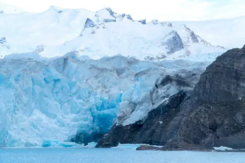 Getty Images A large glacier next to a large rock, with a river basin below