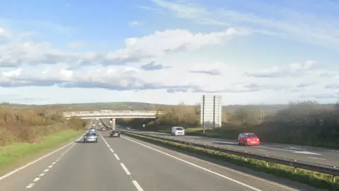 A dual carriageway on the left and another on the fight with some cars and a signpost.