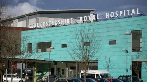 The front of Gloucestershire Royal Hospital which is turquoise blue and has the name of the hospital in big white letters on the roof