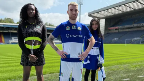 Three models show off the recycled football kits at a clothes show on the pitch at Blackburn Rovers' Ewood Park stadium
