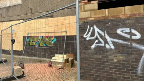 Chaz Fenner A boarded-up building with fencing in front of it.