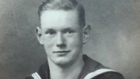 The Redston family Bill Redston in a black and white image dressed in a Royal Navy uniform. He has short, dark hair with a side parting and is clean shaven.