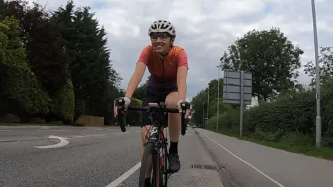 Rebecca Laurel/PA Wire Rebecca Laurel, a 25-year-old woman, riding a bike on a road wearing an orange and purple cycling jersey and a white helmet.