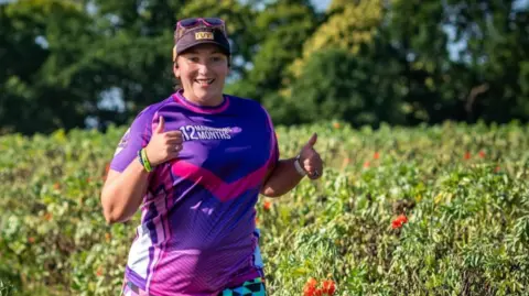 Sarah King The image shows a woman running in a field at a Nature Reserve; she is wearing running gear including a hat and sunglasses.