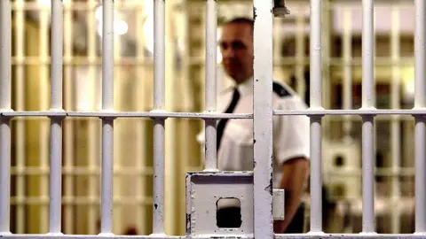 A prison guard at HMP Pentonville stands behind a locked gate 