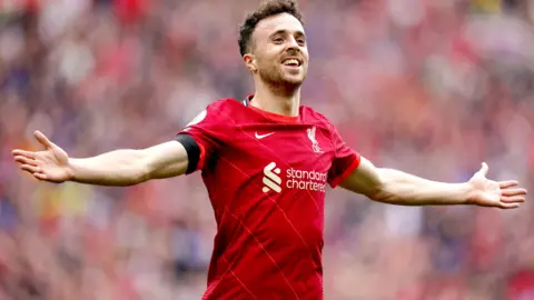 Diogo Jota celebrates scoring a goal with his arms outstetched playing for Liverpool in their red home kit in 2021.