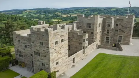National Trust A castle in a light coloured stone with rolling hills in the background.