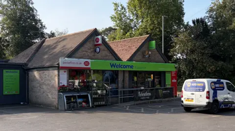 A small Co-op convenience store is pictured with a van in the car park. The branding is lime green and it has a Post Office attached to it.