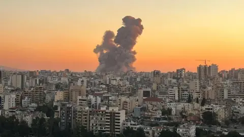 Alaa Ghalayini The skyline of Beirut, with a plume of smoke seen rising up on the horizon against a burnt orange skyline. 