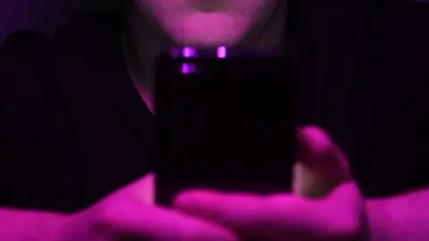 James Chapelard/Crimestoppers Illustrative photograph showing a close-up of a mobile phone being held in an unidentifiable man's hands while he watches the screen.