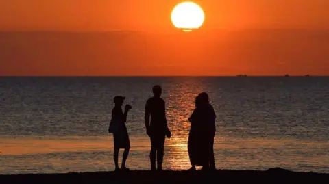 silhouettes on a beach in front of the sea as the sun sets