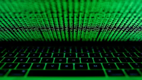 A computer keyboard with black keys illuminated in green. There are random digits in green scrolling down the screen