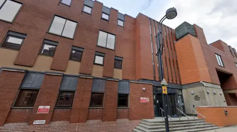 Google Exterior of a red brick building with a sign saying Leeds Combined Courts near a black-framed entrance door.